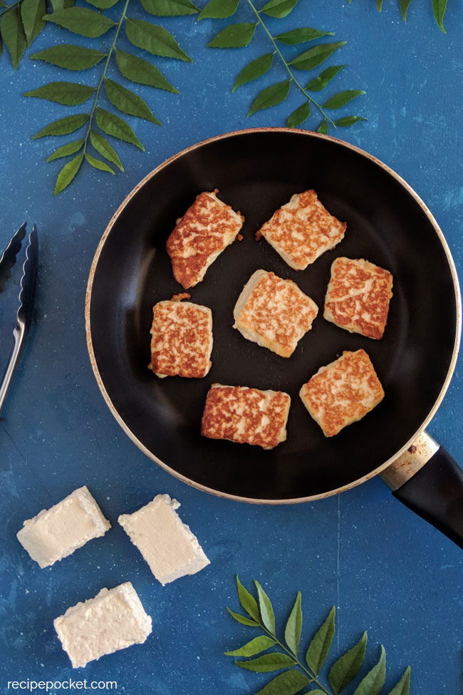 Fried paneer cubes in no stick fry pan, surrounded by fresh curry leaves.