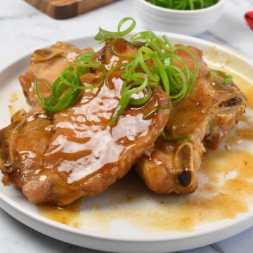 Pork chops in gravy with spring onion curls.