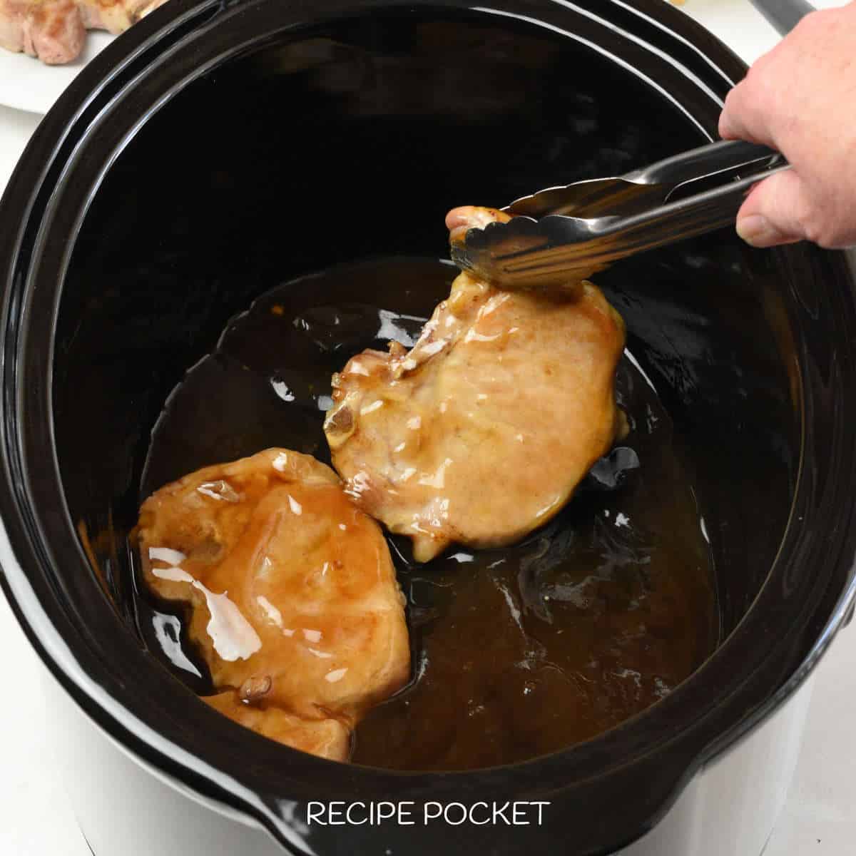 Two pork chops in a black slow cooker bowl.