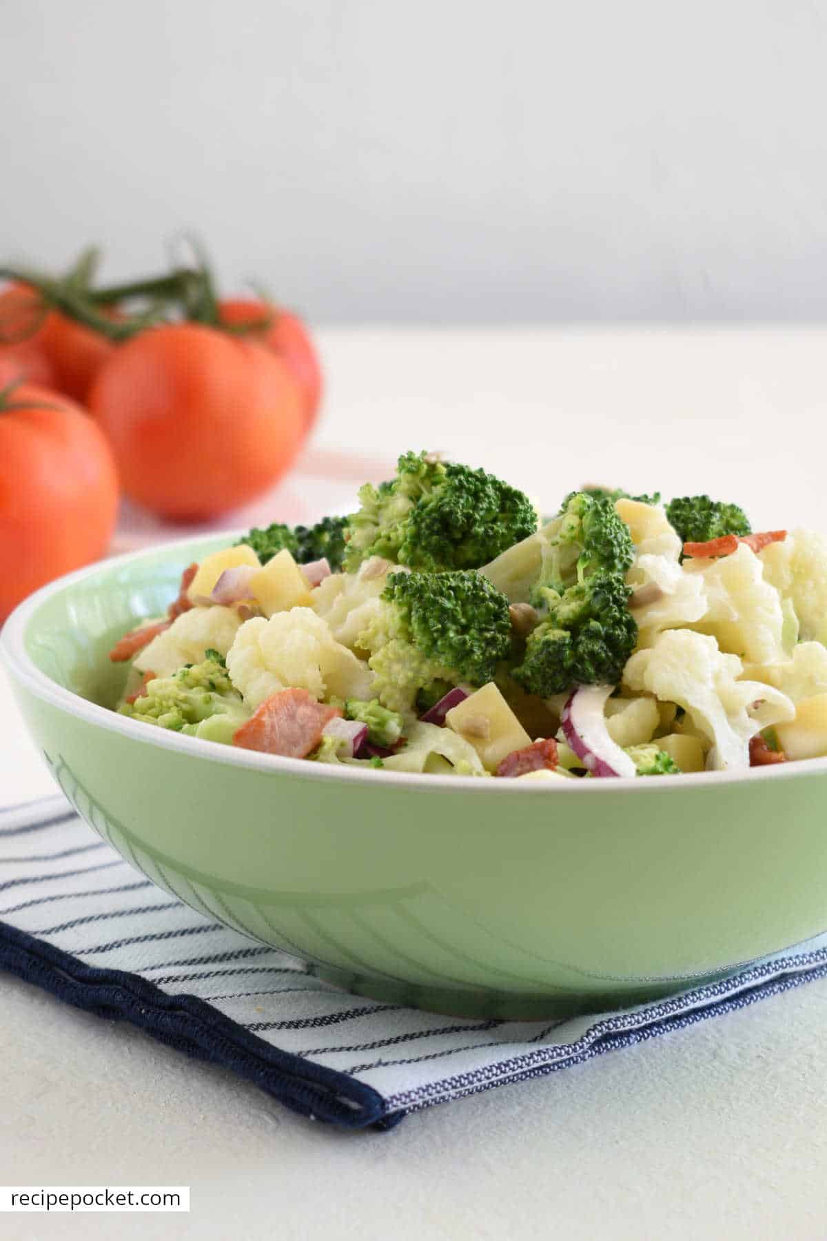 Salad in a green bowl with vine ripened tomatoes in the background.