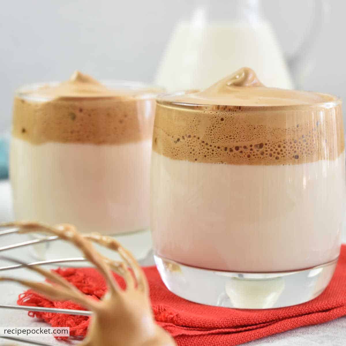 Close up of dalgona iced coffee with whisk in foreground.