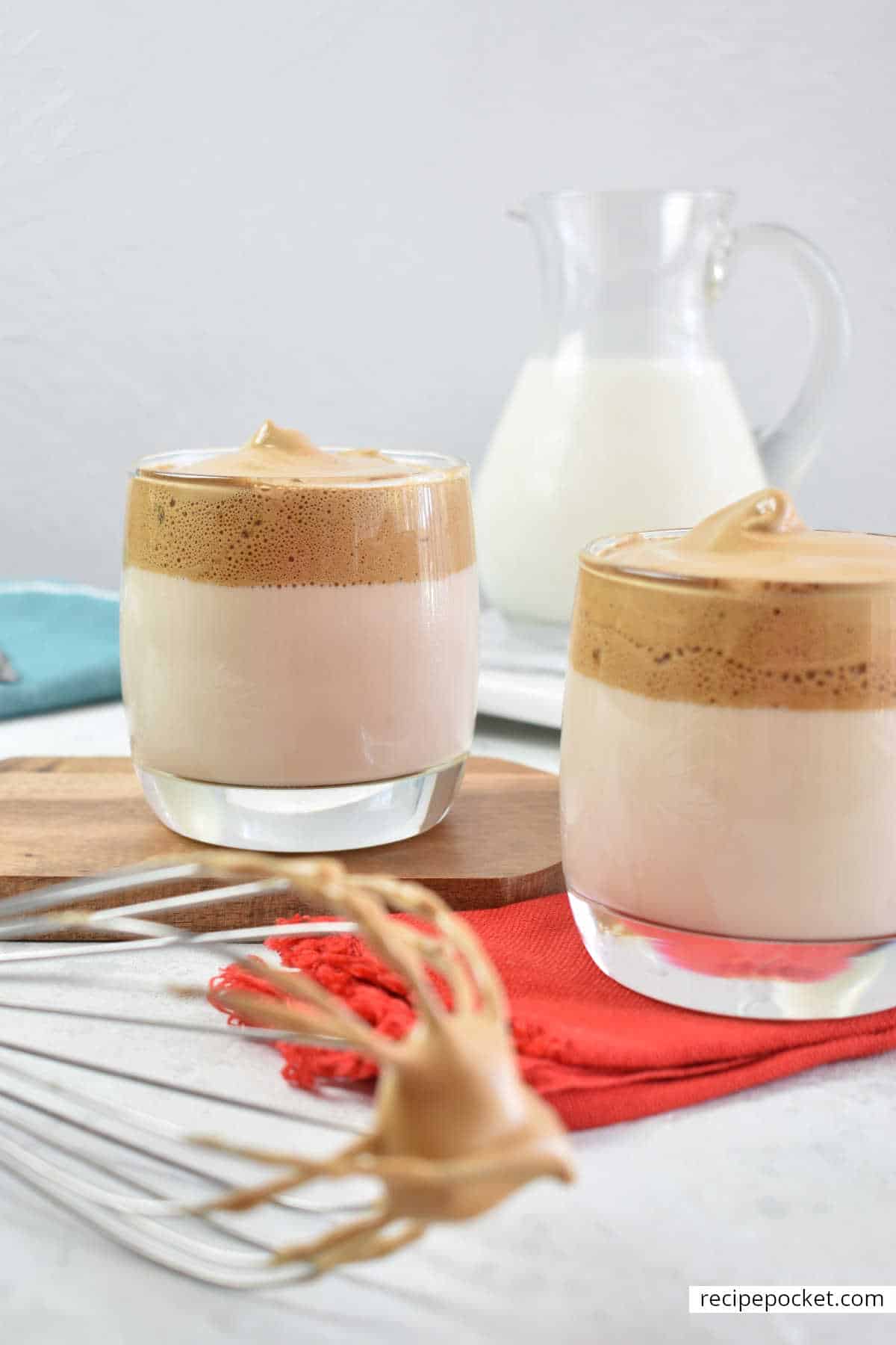 Two glasses of iced coffee with milk jug in the background.