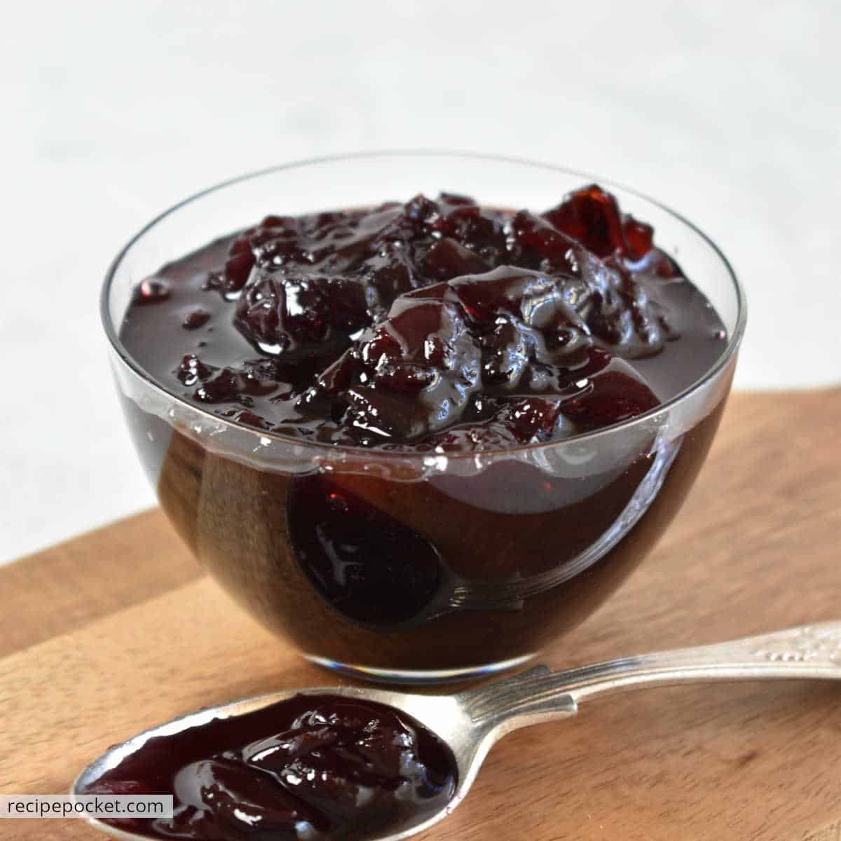 Morello jam in a glass bowl on a wooden board.