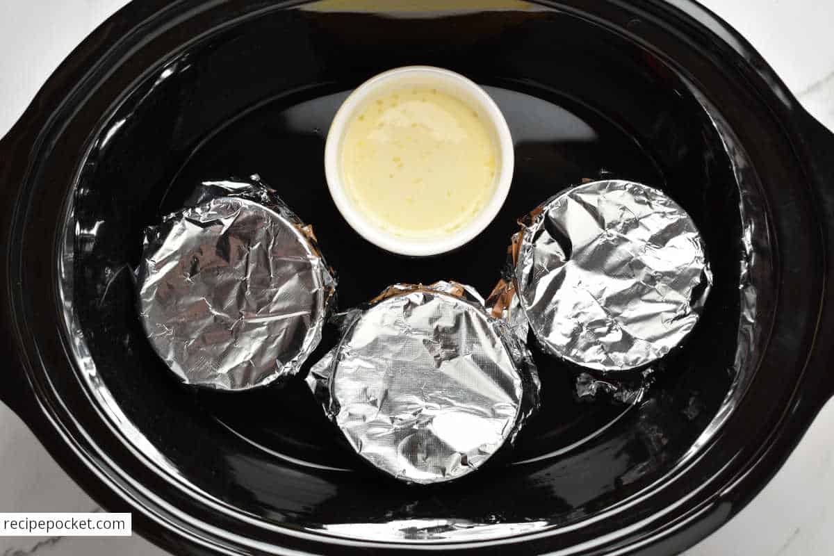 Ramekins with unbaked custard in a slow cooker bowl filled with water.