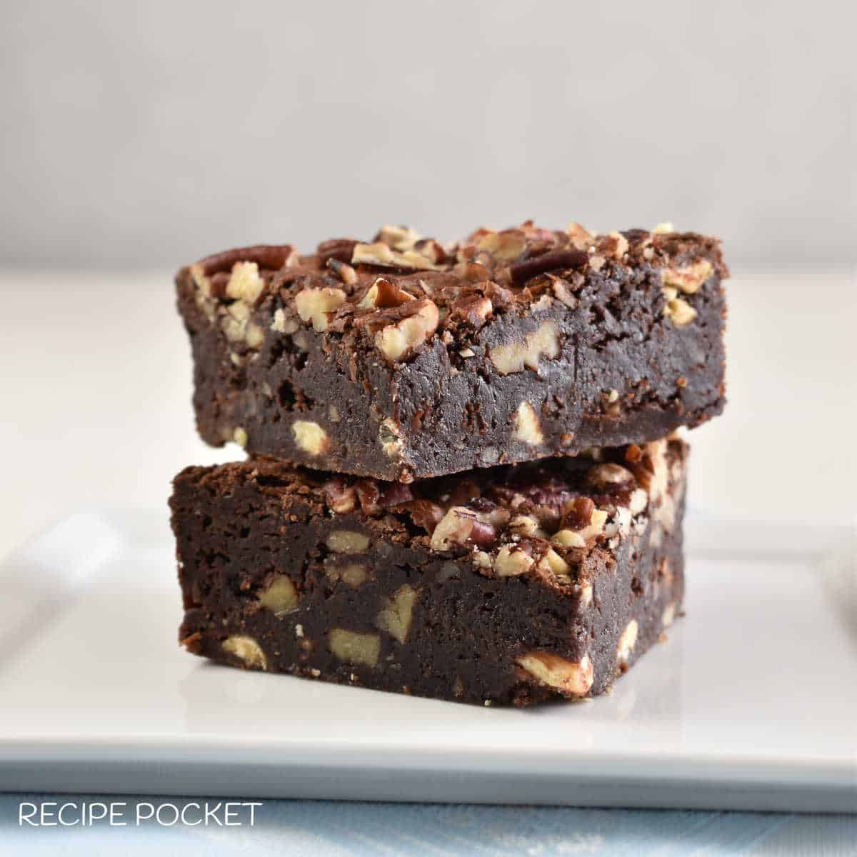 Two brownies with pecans on a white plate.