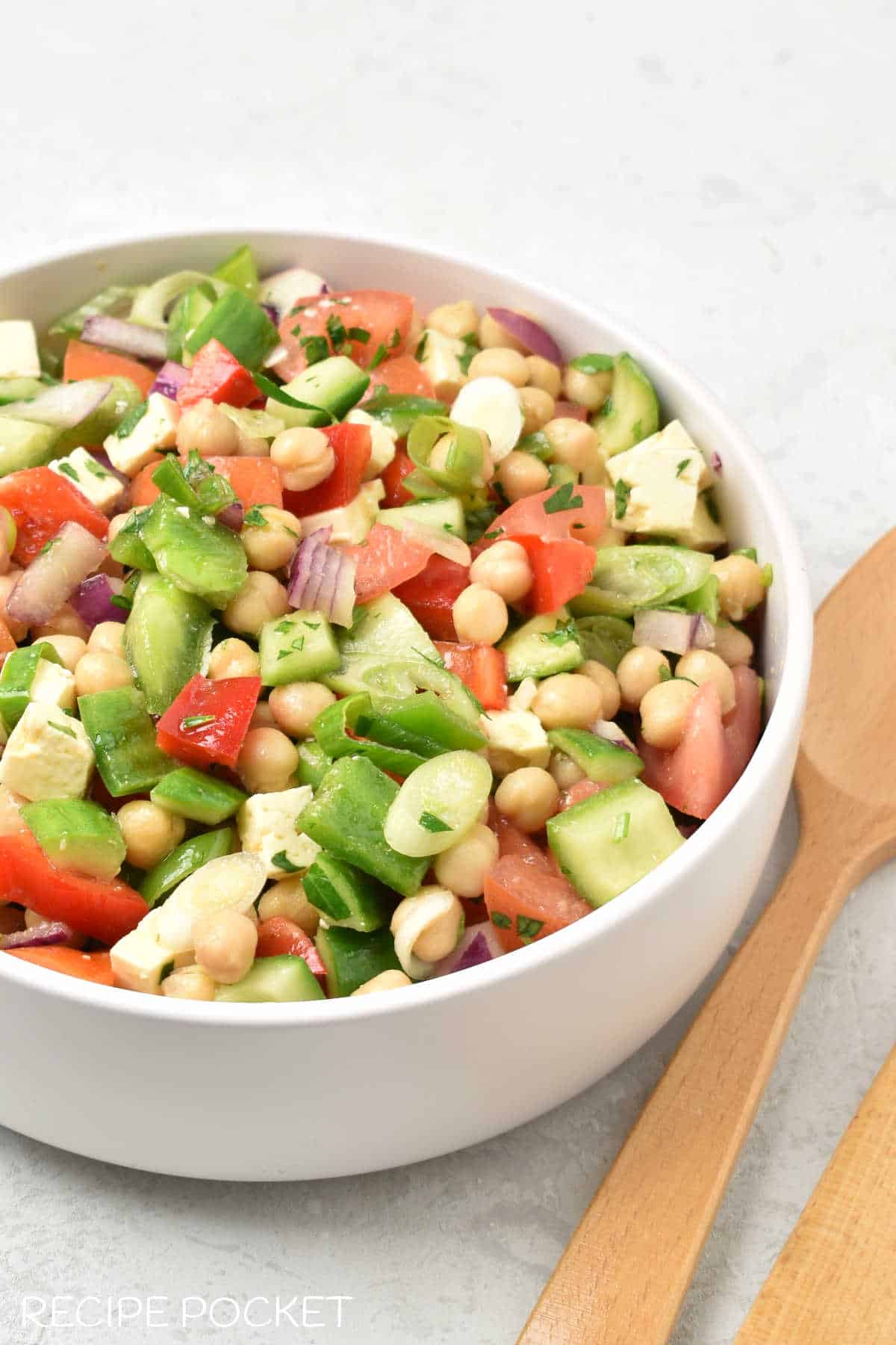 A forty five degree angle image of Greek salad with wooden serving spoons.