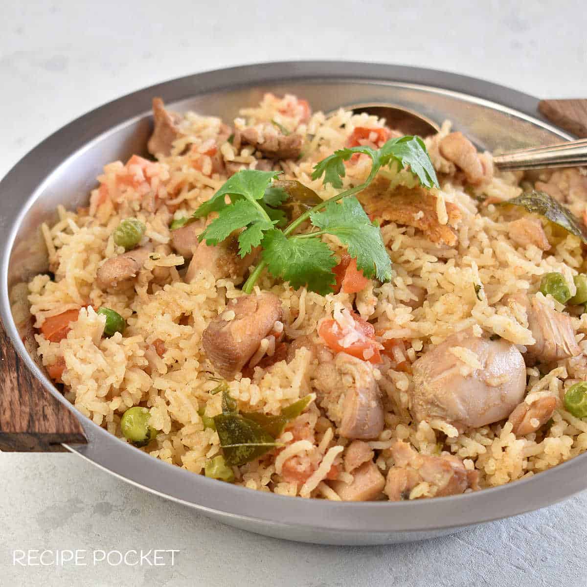 A close up of one pot chicken and rice in a silver bowl with a spoon.