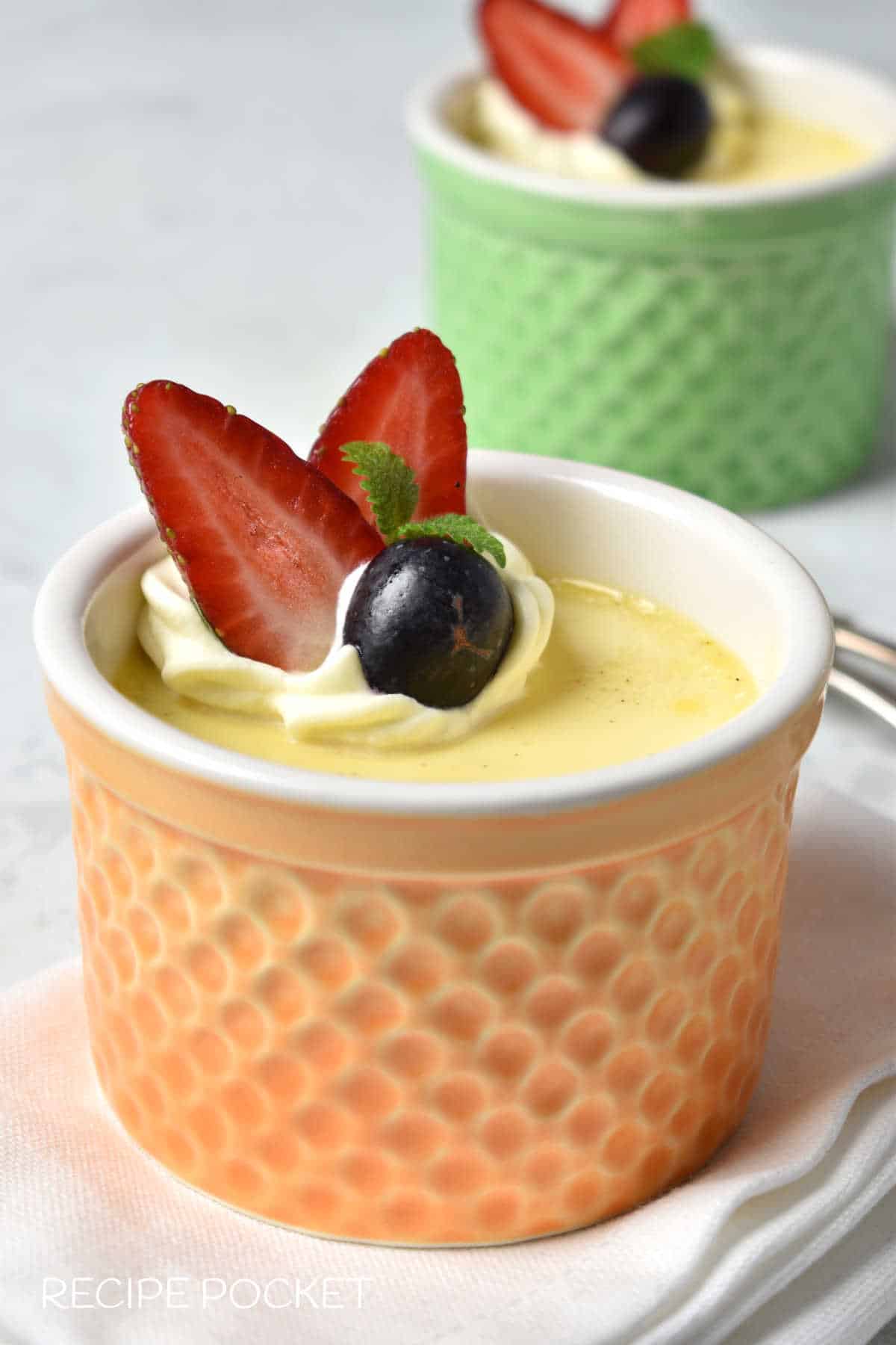 Custard with cream and strawberries in an orange ramekin.