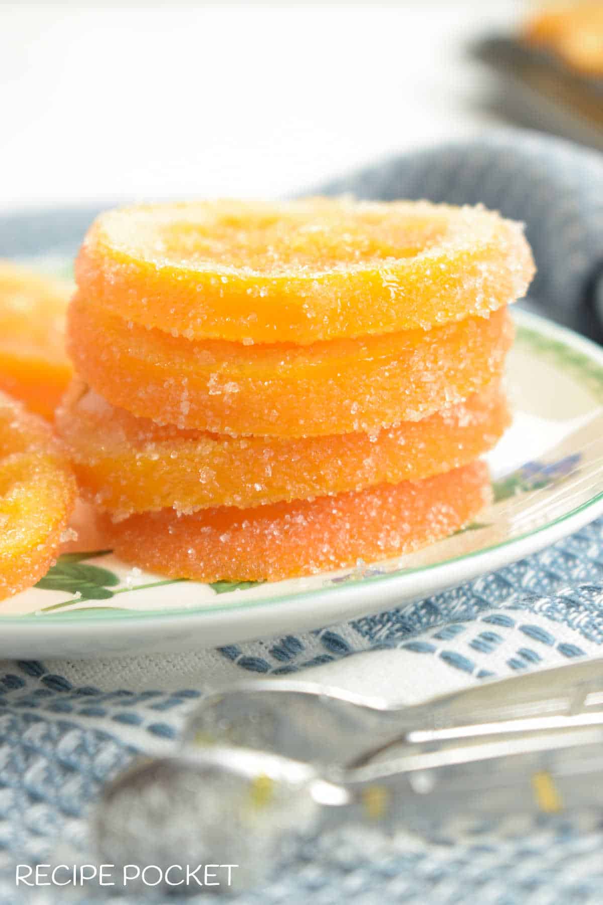 Slices of candied oranges on a plate with tongs in the forground.