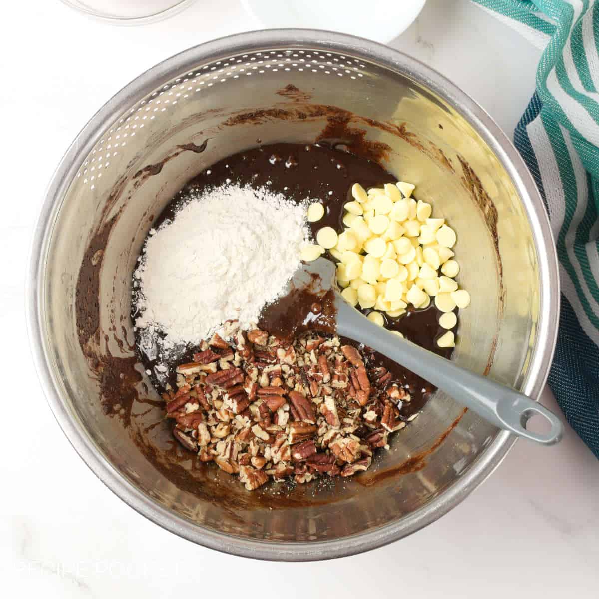 Flour, white chocolate chips, and nuts in a bowl with melted chocolate.