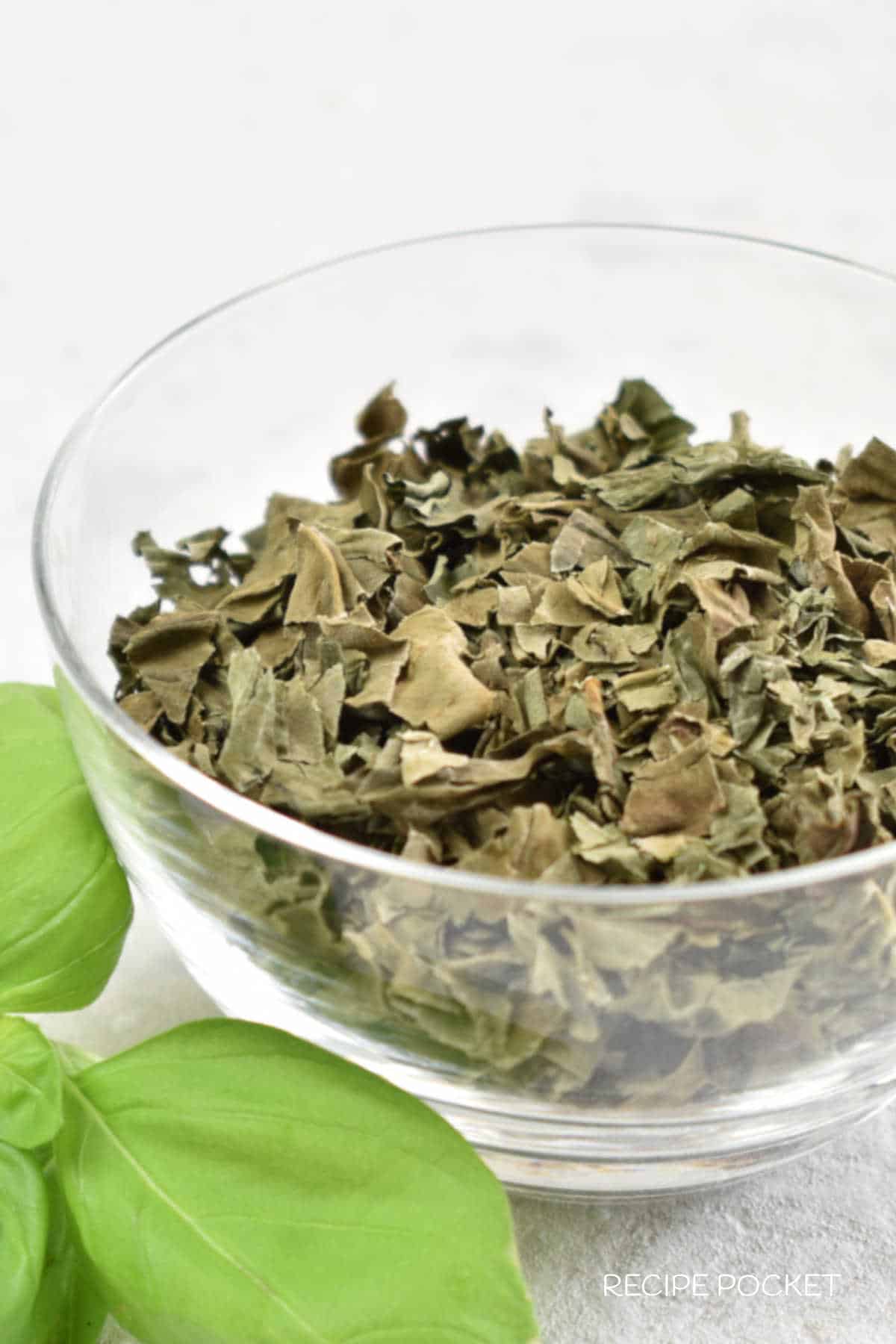 Homemade dried basil cut into small pieces in a glass bowl.