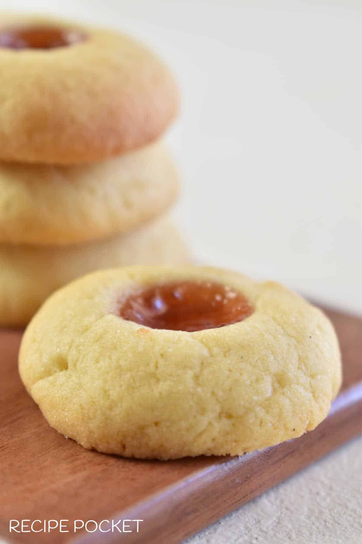 A closeup of a single jam drop cookie on a wooden board.