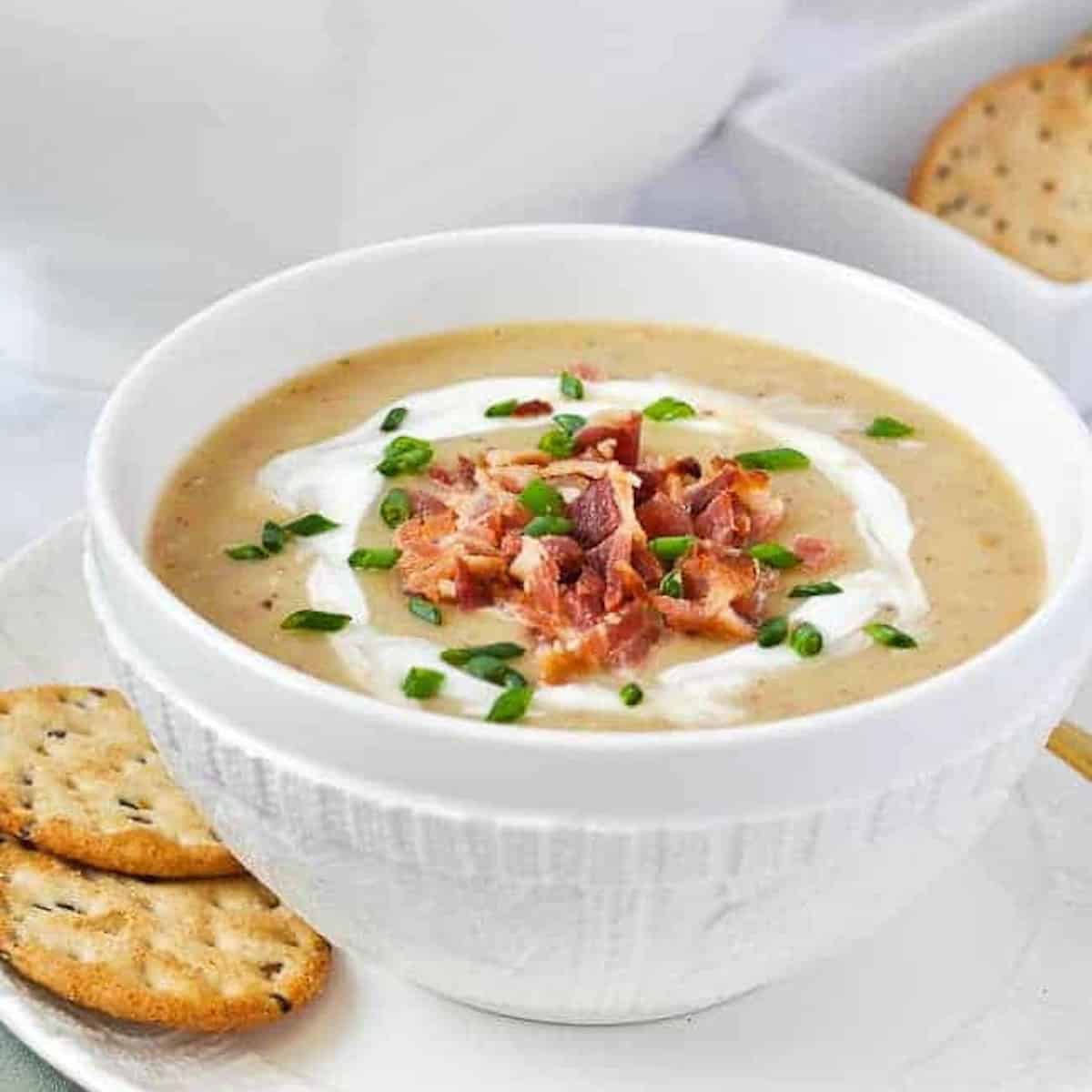 A white bowl with potato and leek soup garnished with crispy bacon bits.