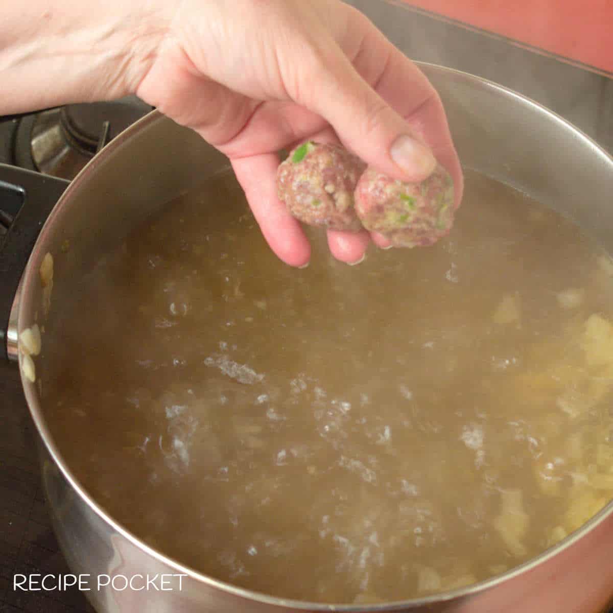 Raw meat balls being placed into soup.