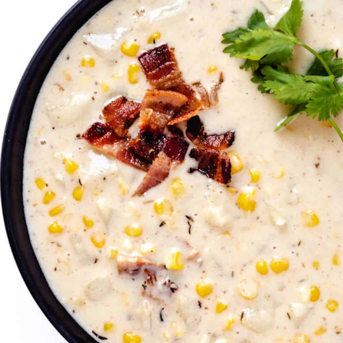 Potato and corn chowder garnished with bacon and parsley in a black bowl.