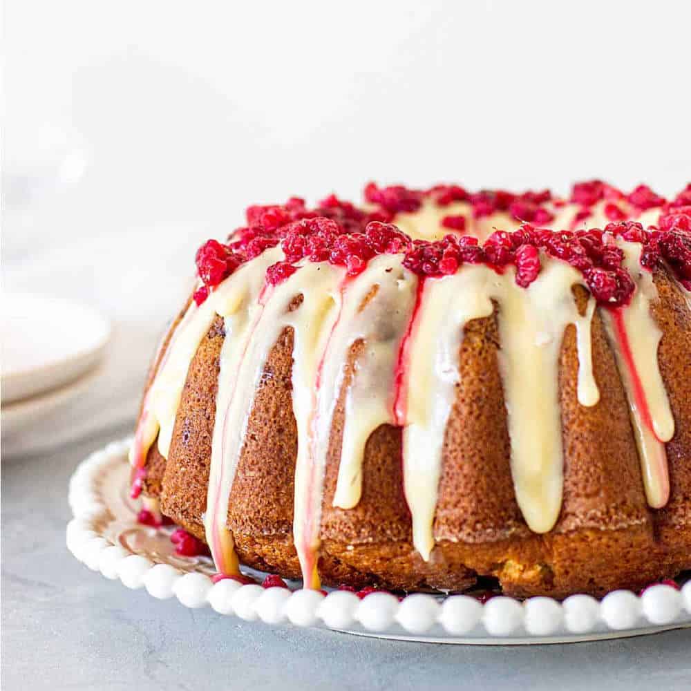 Side view of a bundt cake with drip icing and raspberries on top.