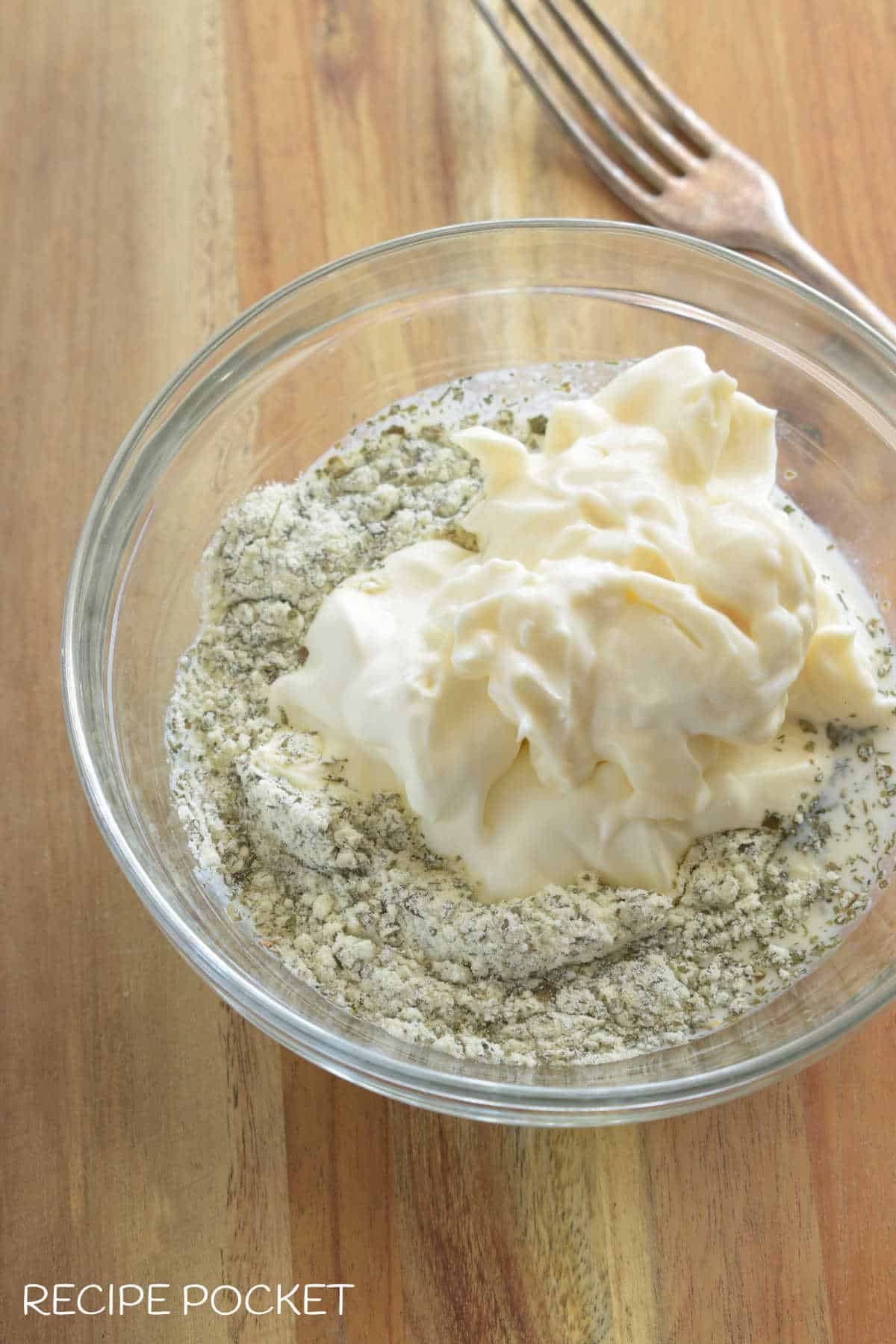 Dry ranch dressing mix in a small bowl with mayo, sour cream and milk.