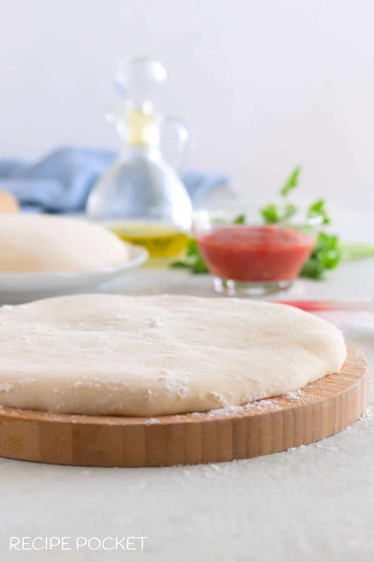 A close up of pizza dough on a wooden board.