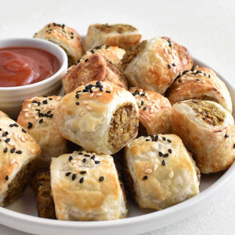 Puff pastry sausage rolls on a white plate with a small bowl of tomato sauce.
