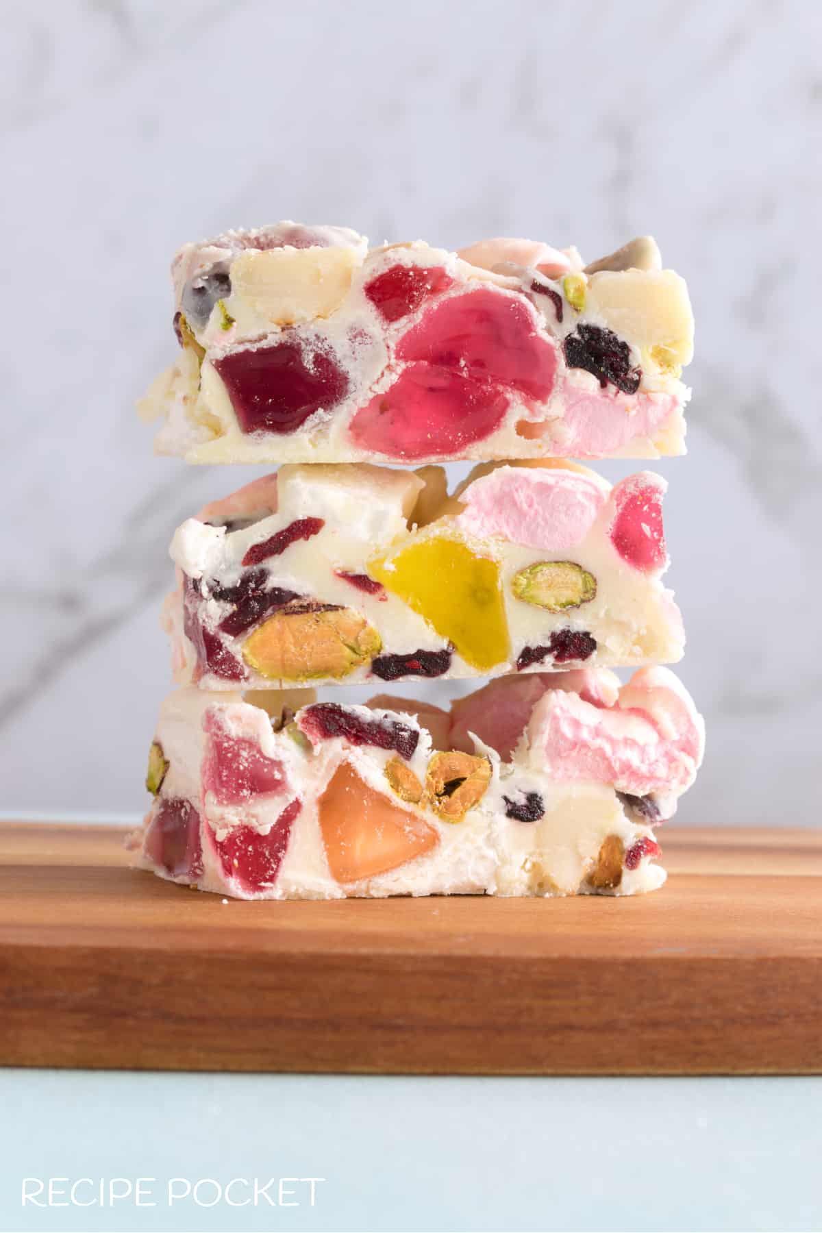 Three pieces of white chocolate rocky road on a wooden board.