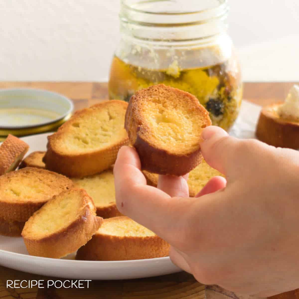 A closeup of a piece of baguette crostini being held by a hand.