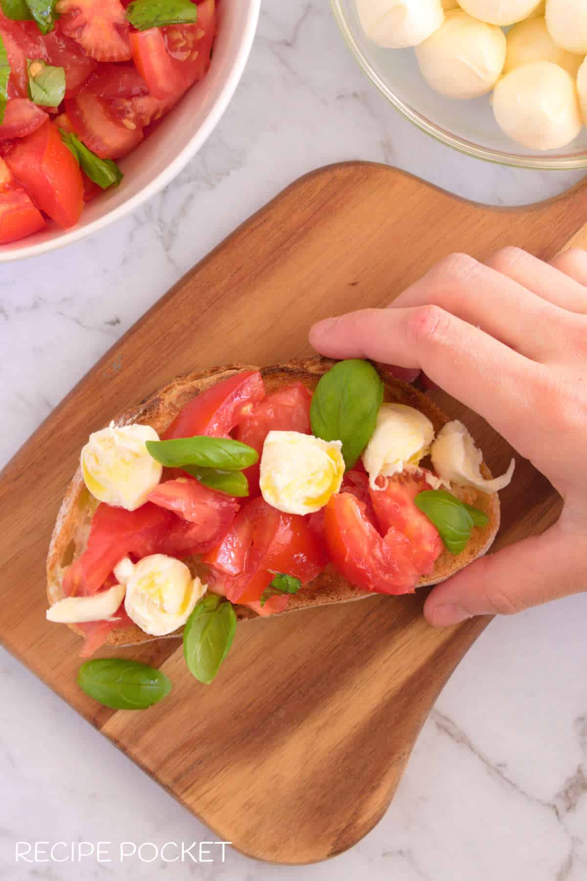 A hand picking up a bruschete with mozzerella.