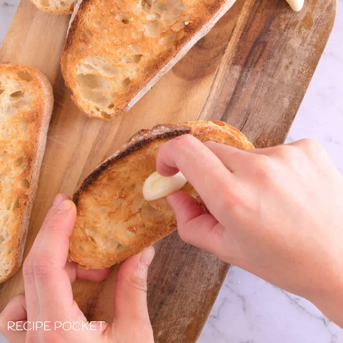 Raw garlic being wiped onto toasted bread.