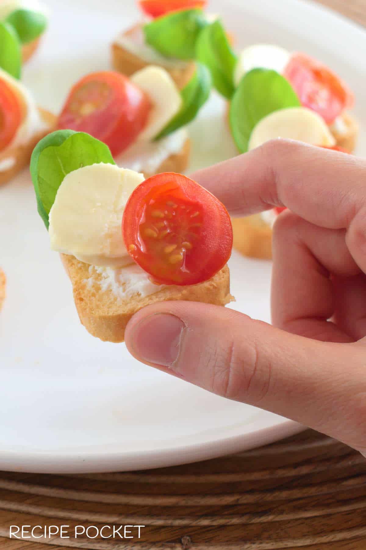 A hand holding a piece of caprese crostini.