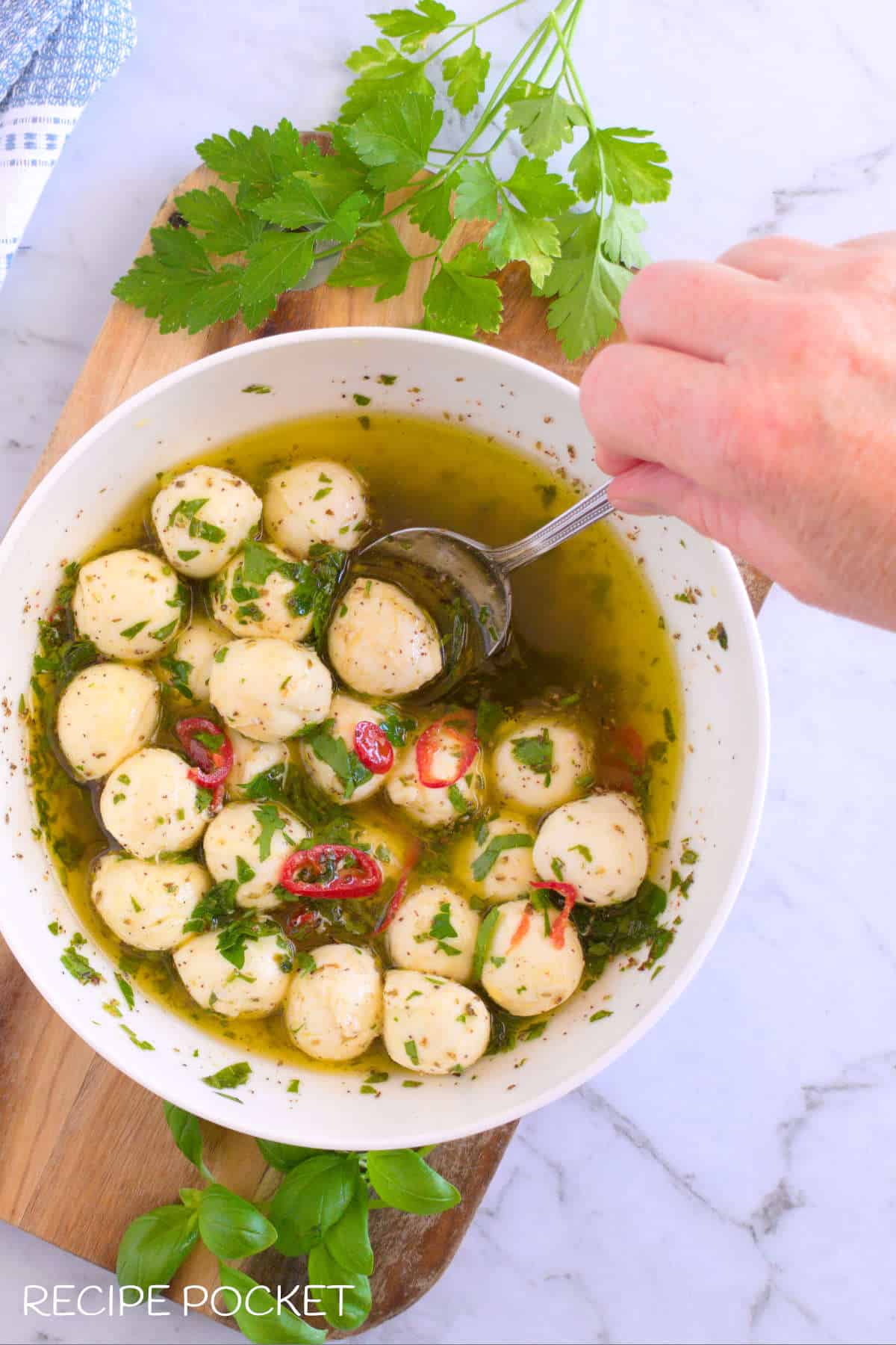 Mozzarella balls being stirred into an olive oil herb mix.