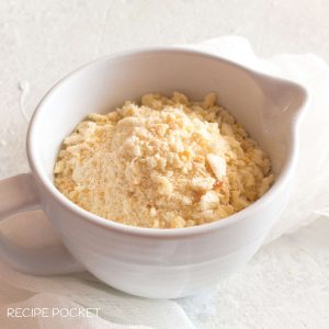 A white jug filled with breadcrumbs on a white muslin cloth.