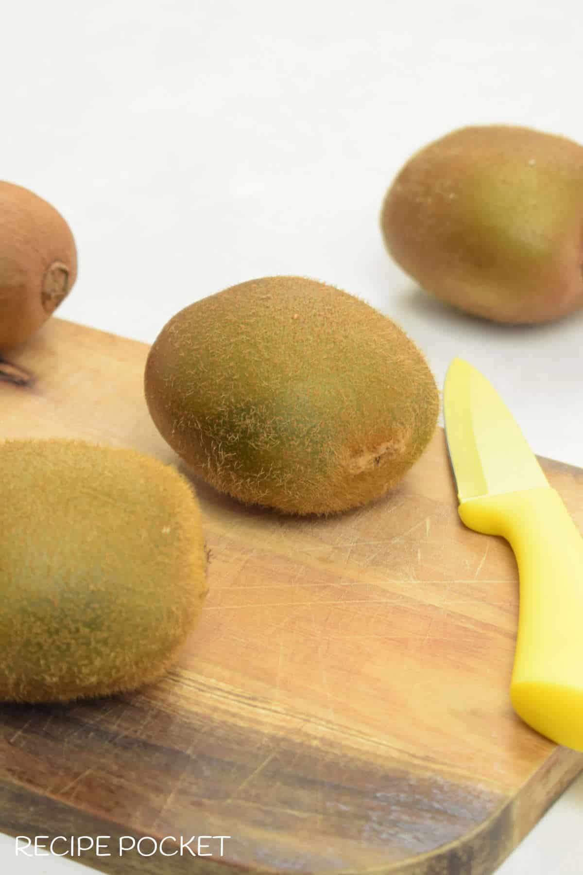 Kiwi fruit on a cutting board with a yellow knife.
