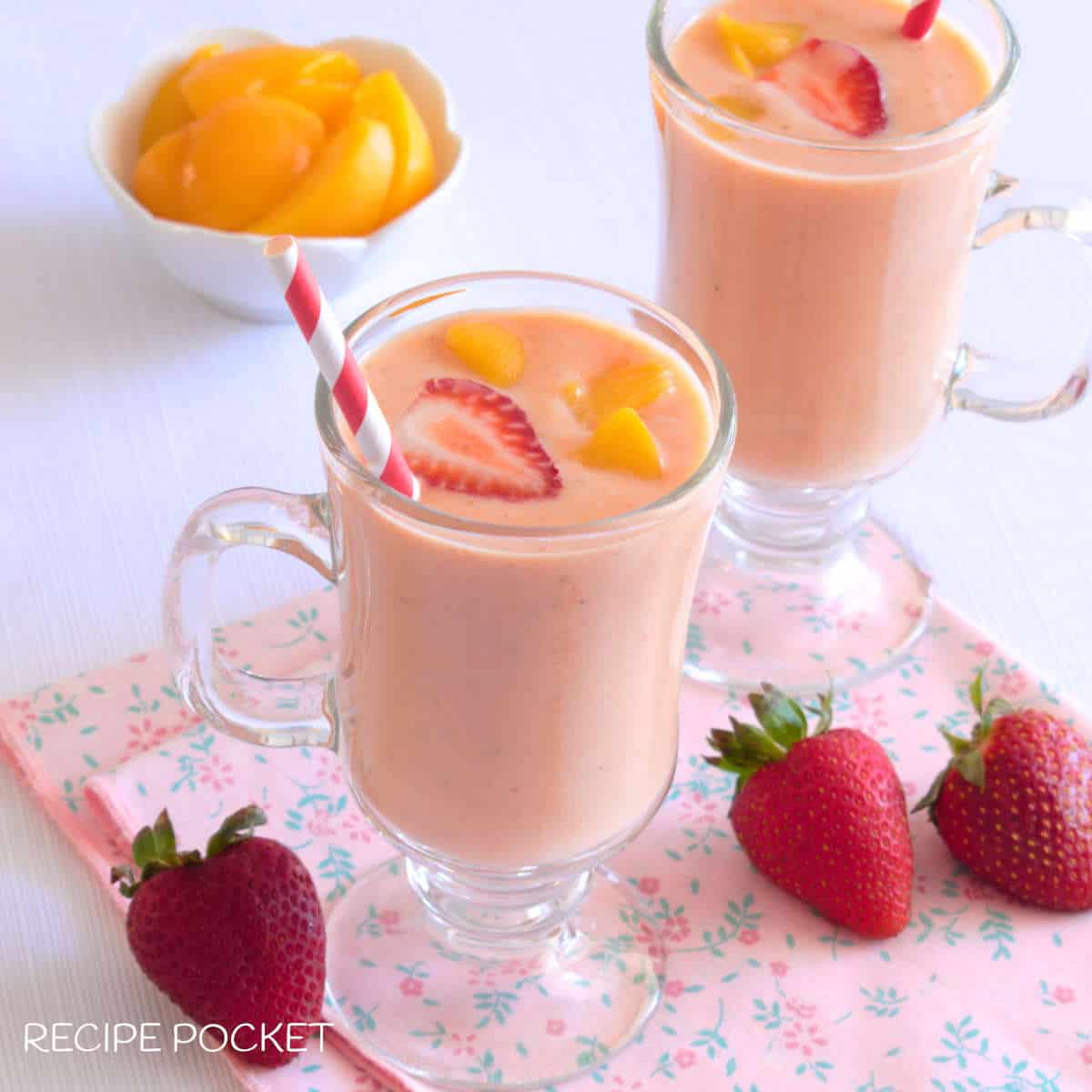 Two glasses with peach and strawberry smoothie garnished with a slice of strawberry and peach pieces.