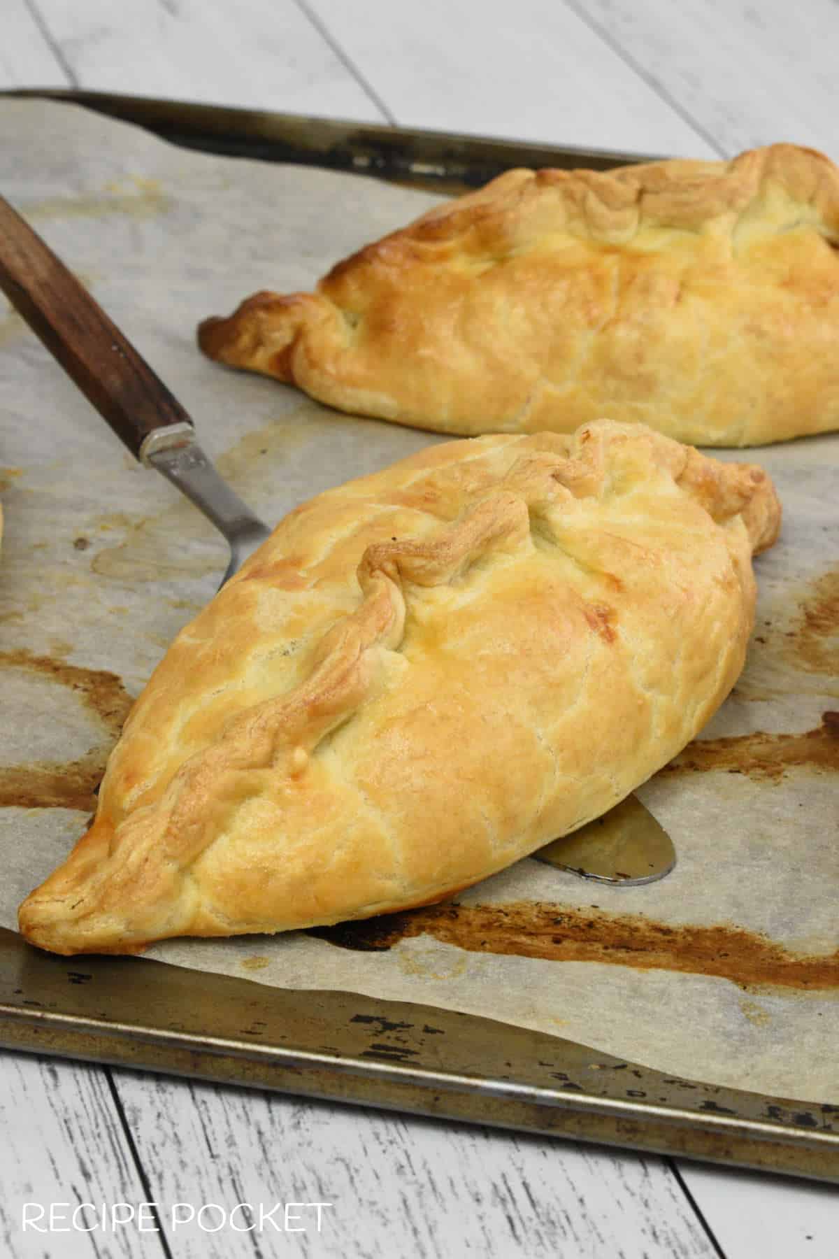 Two Cornish pasties on a baking tray.