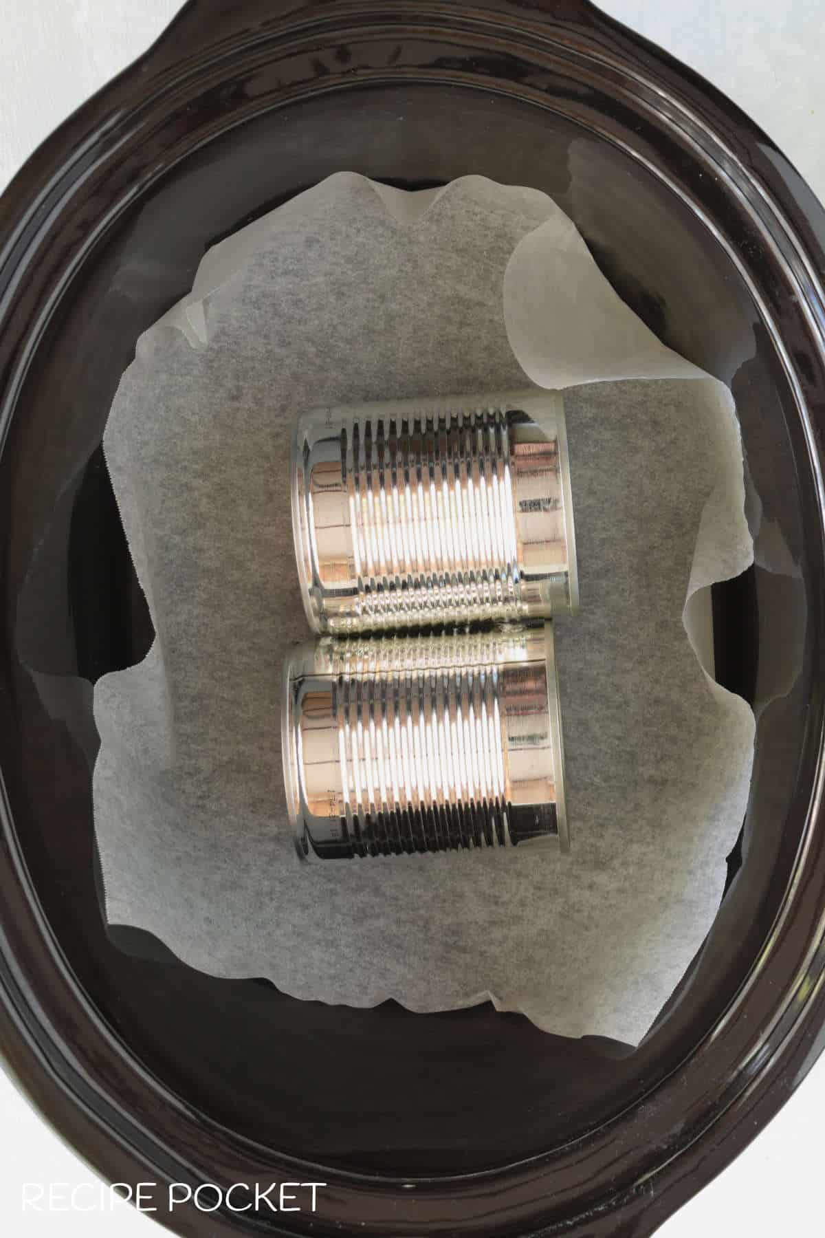Two metal cans in a slow cooker bowl.