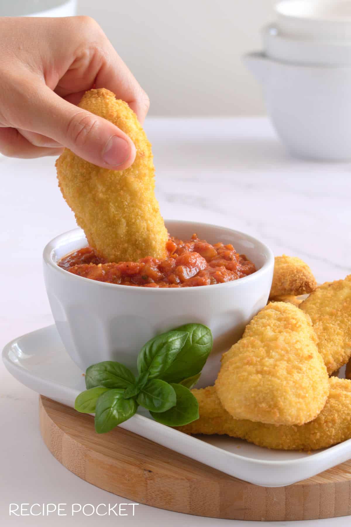 Crumbed chicken being dunked into marinara sauce.