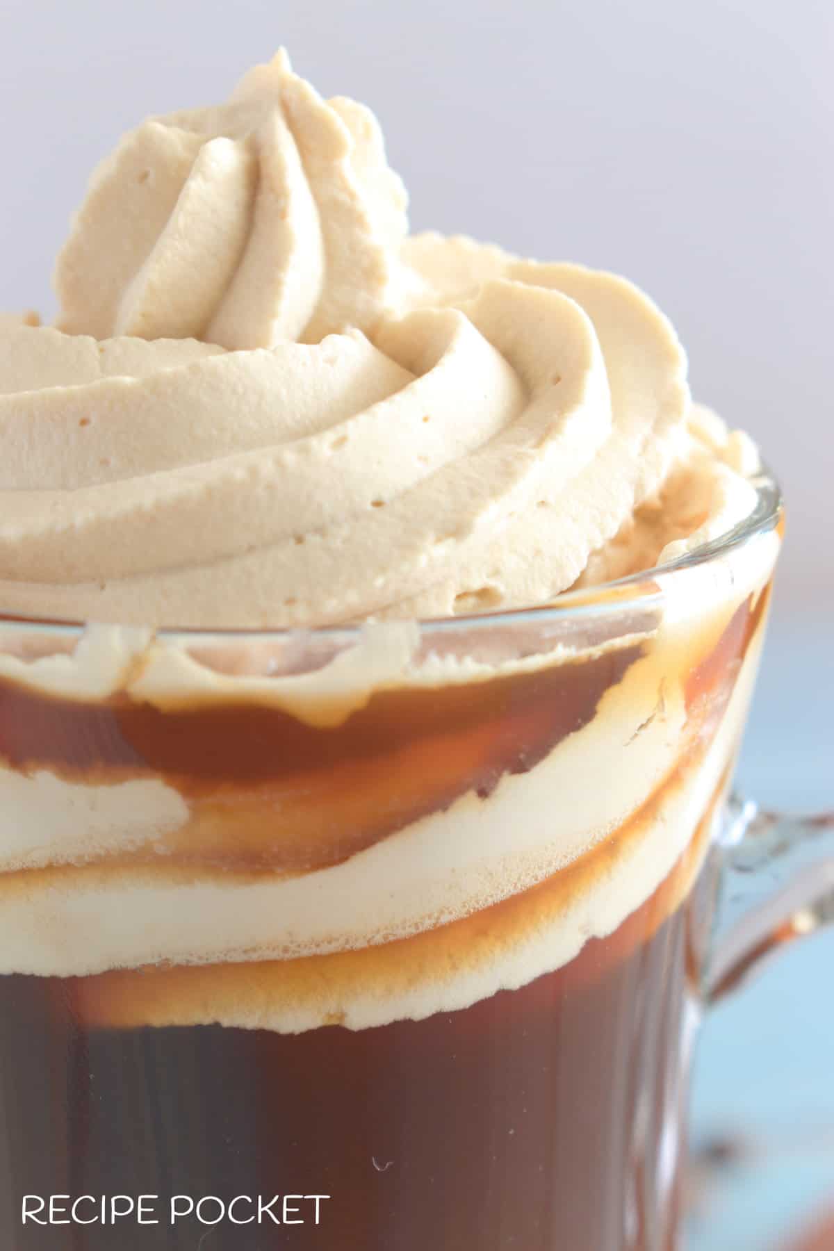 A closeup of coffee whipped cream piped on to coffee in a glass.