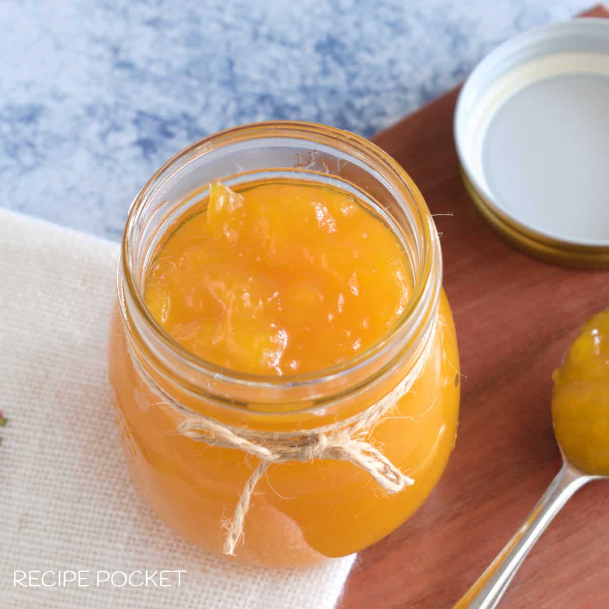 Mango jam in a jar on a wooden board.