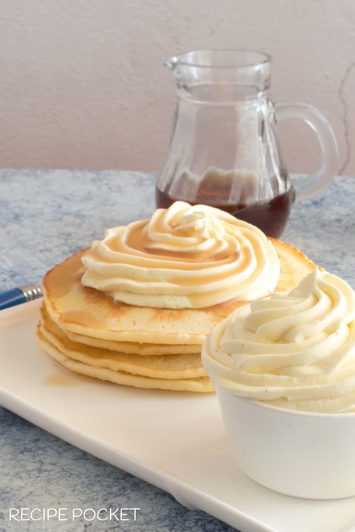 A stack of pancakes with whipped cream and maple syrup on top.
