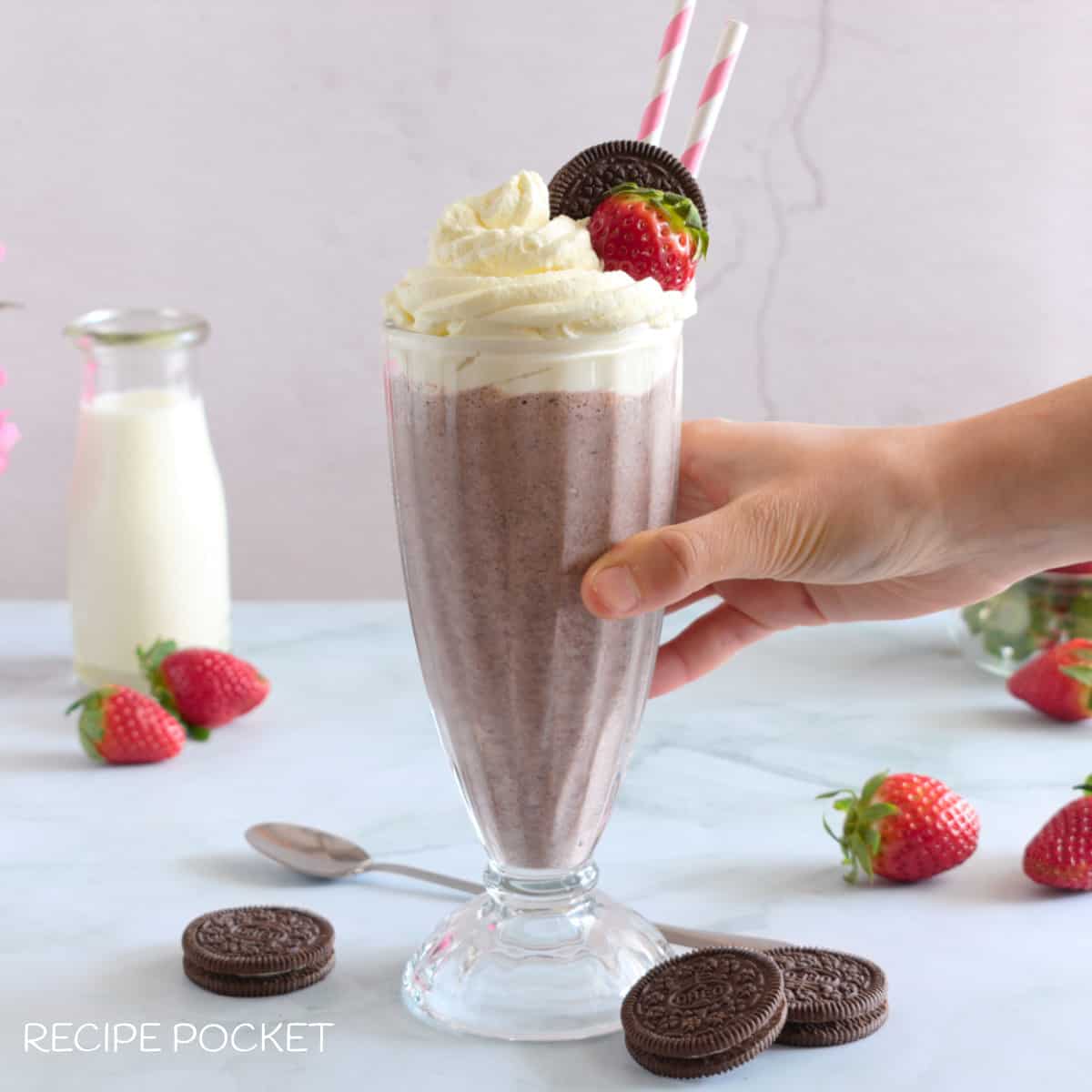 A hand holding a milkshake in a glass.