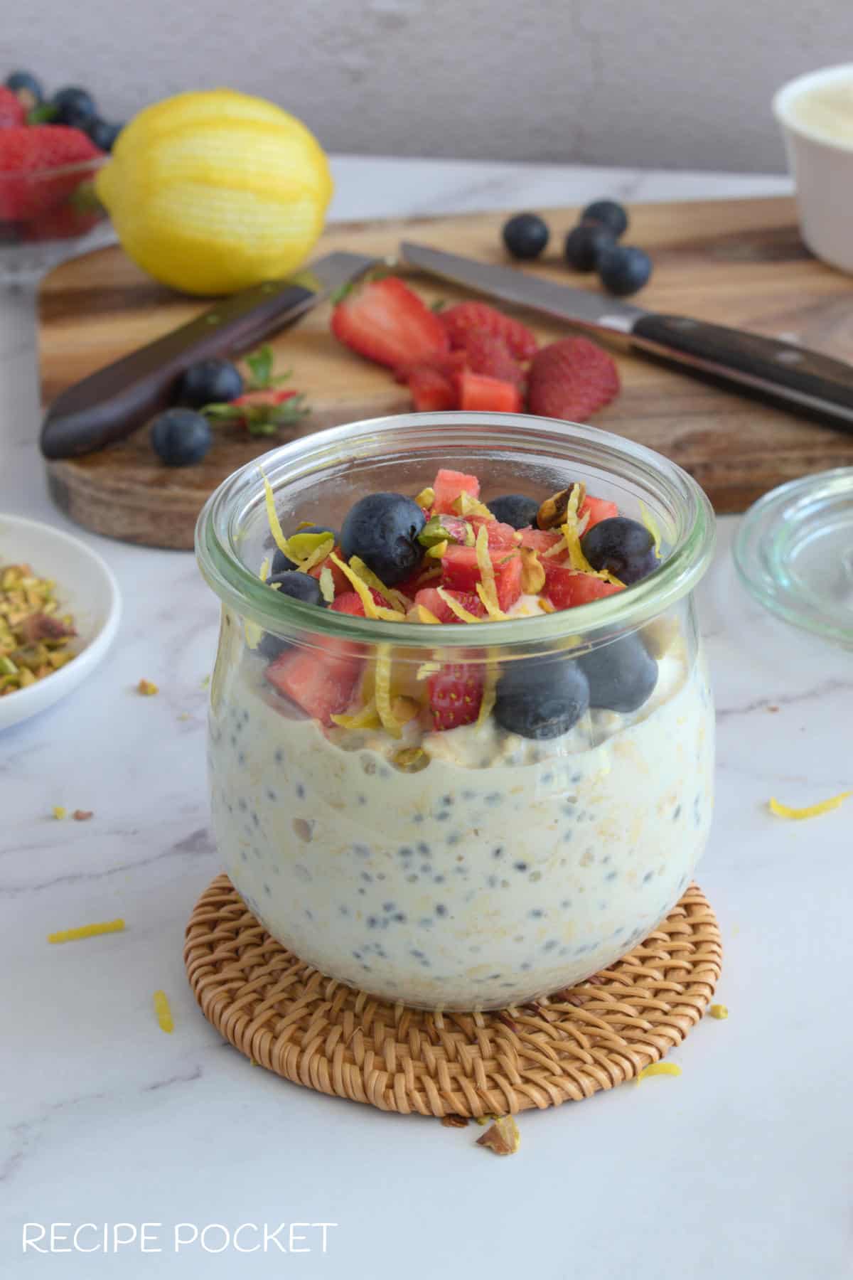 Overnight oats in a jar with a cutting board at the back with fruit on it.