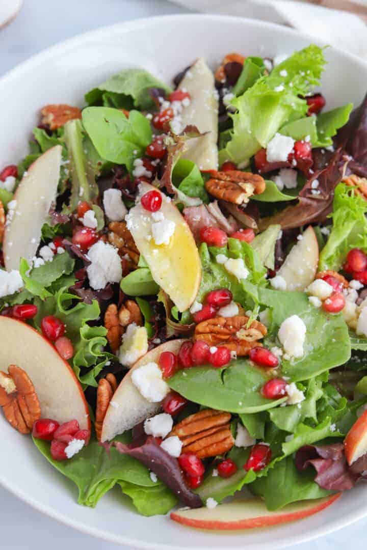 Salad made with apples, pomegrante seeds, green salad leaves and cheese.