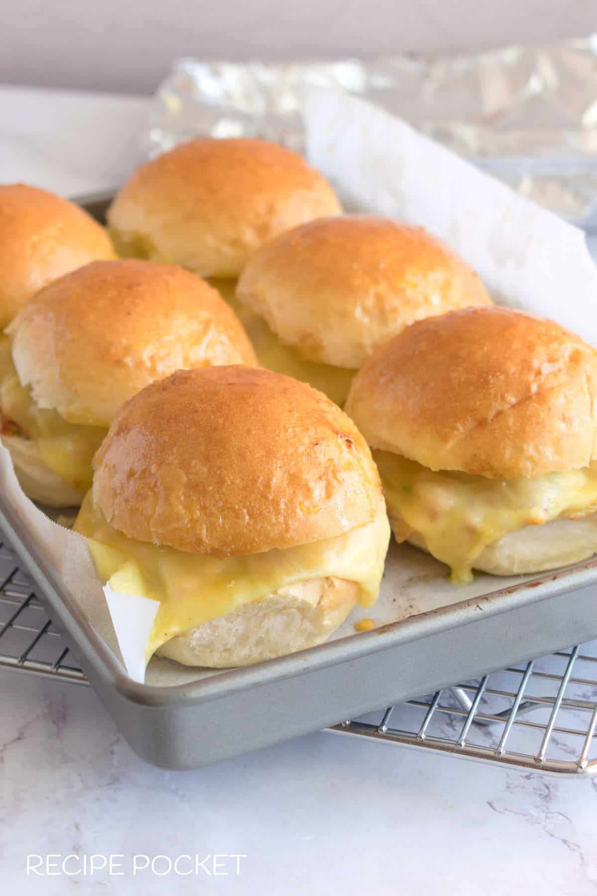 Six baked bbq chicken sliders on a baking tray.