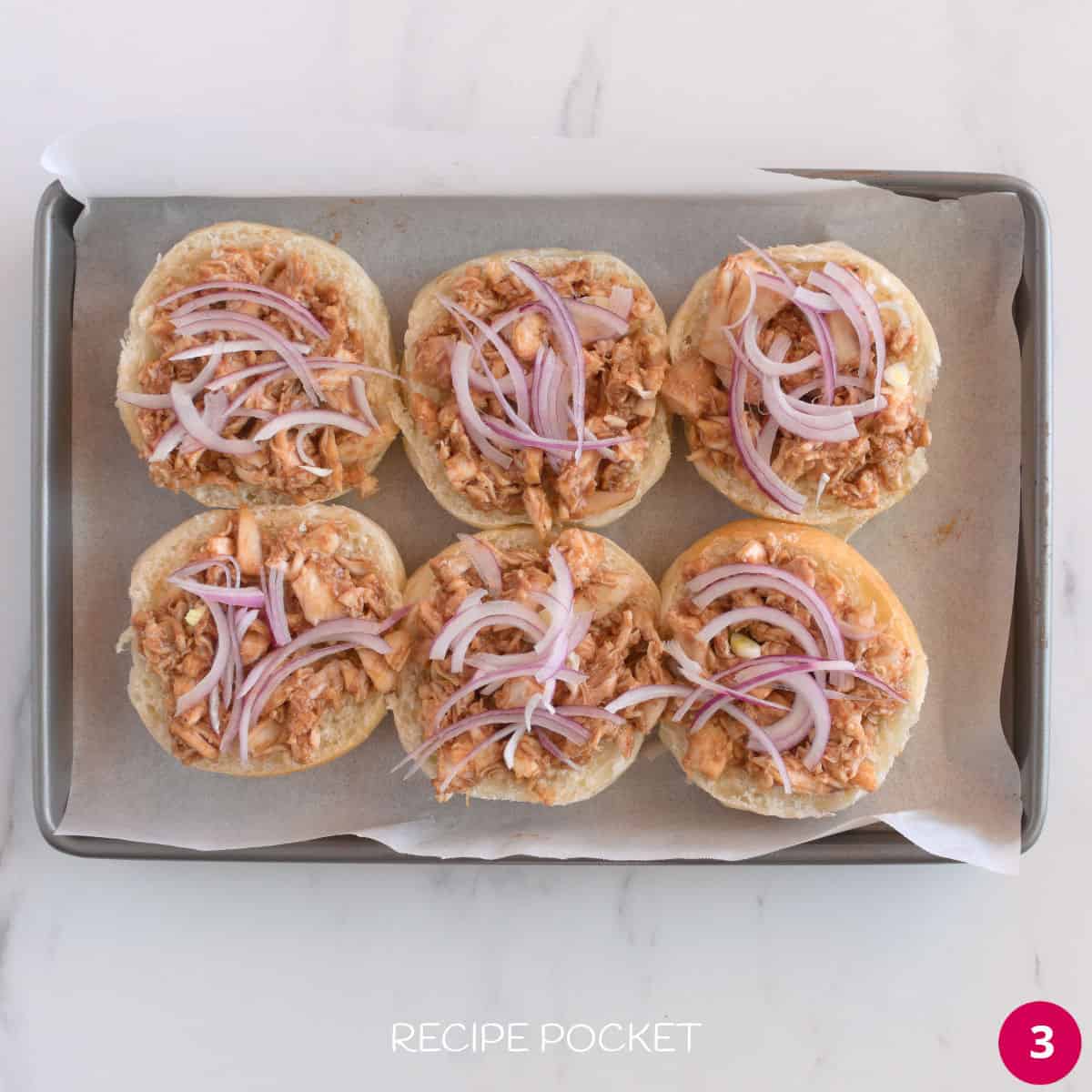 Sliced red onion on top of diced chicken on a bun.