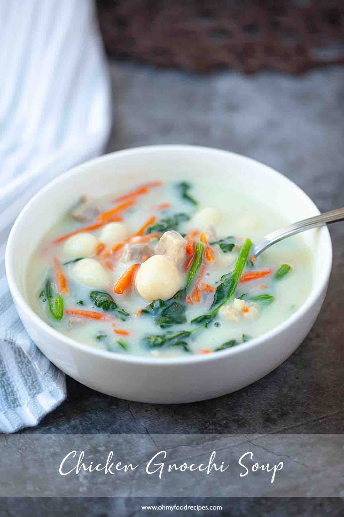 Chicken gnocchi soup in a white bowl on a grey table.