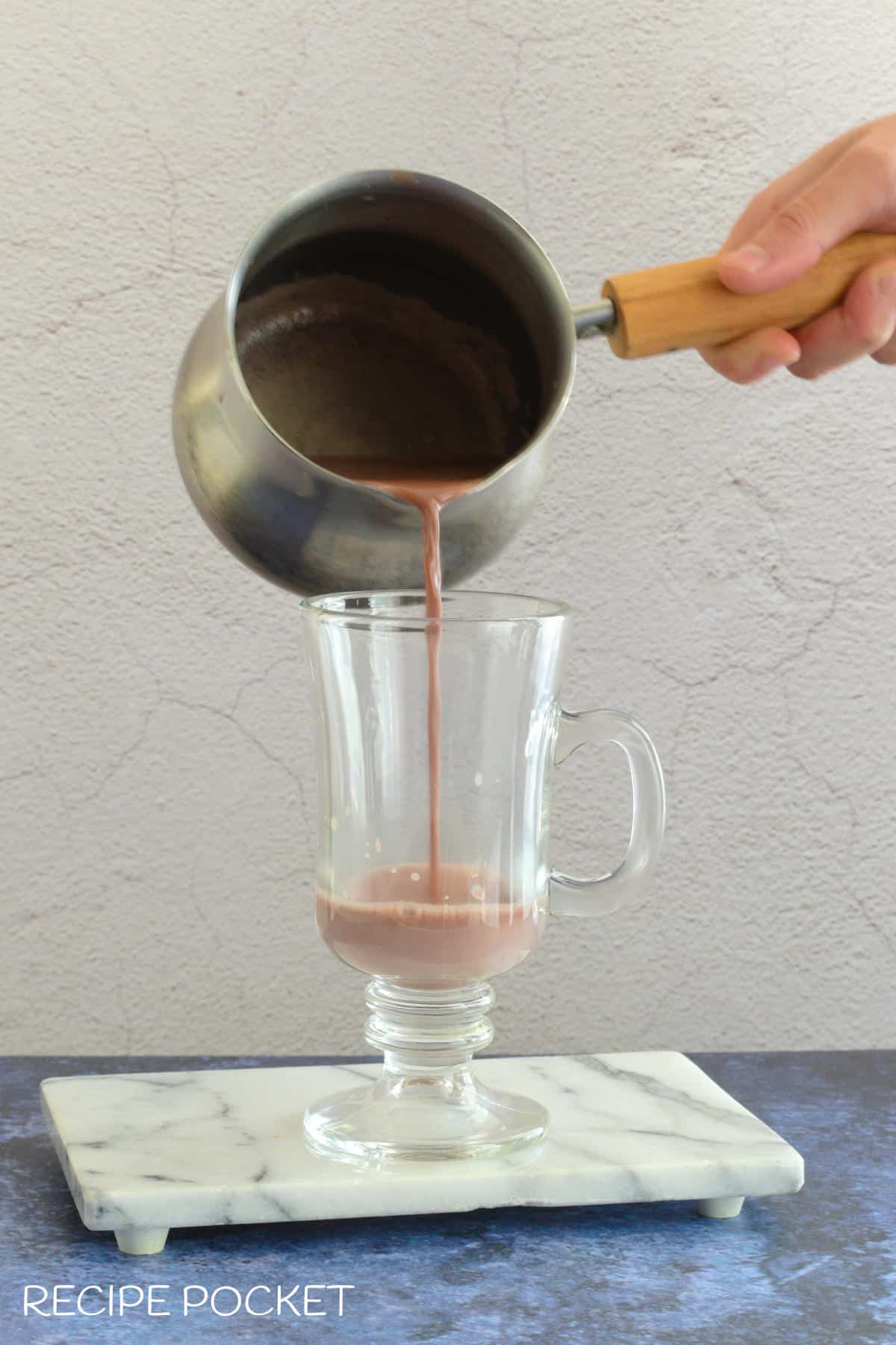 Hot chocolate being poured into a glass mug.