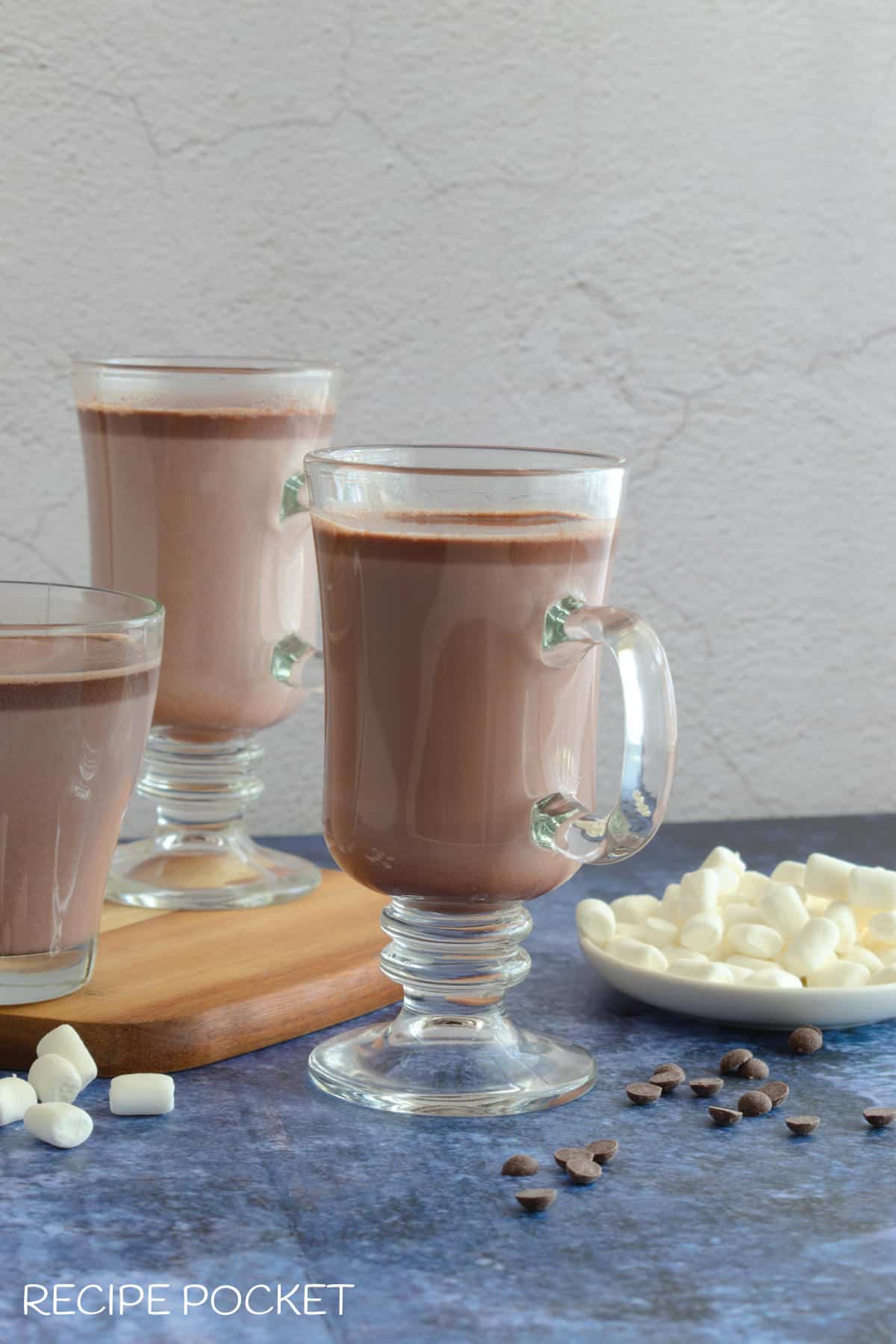 Three mugs of hot chocolate with a plate of marshmallows on the side.