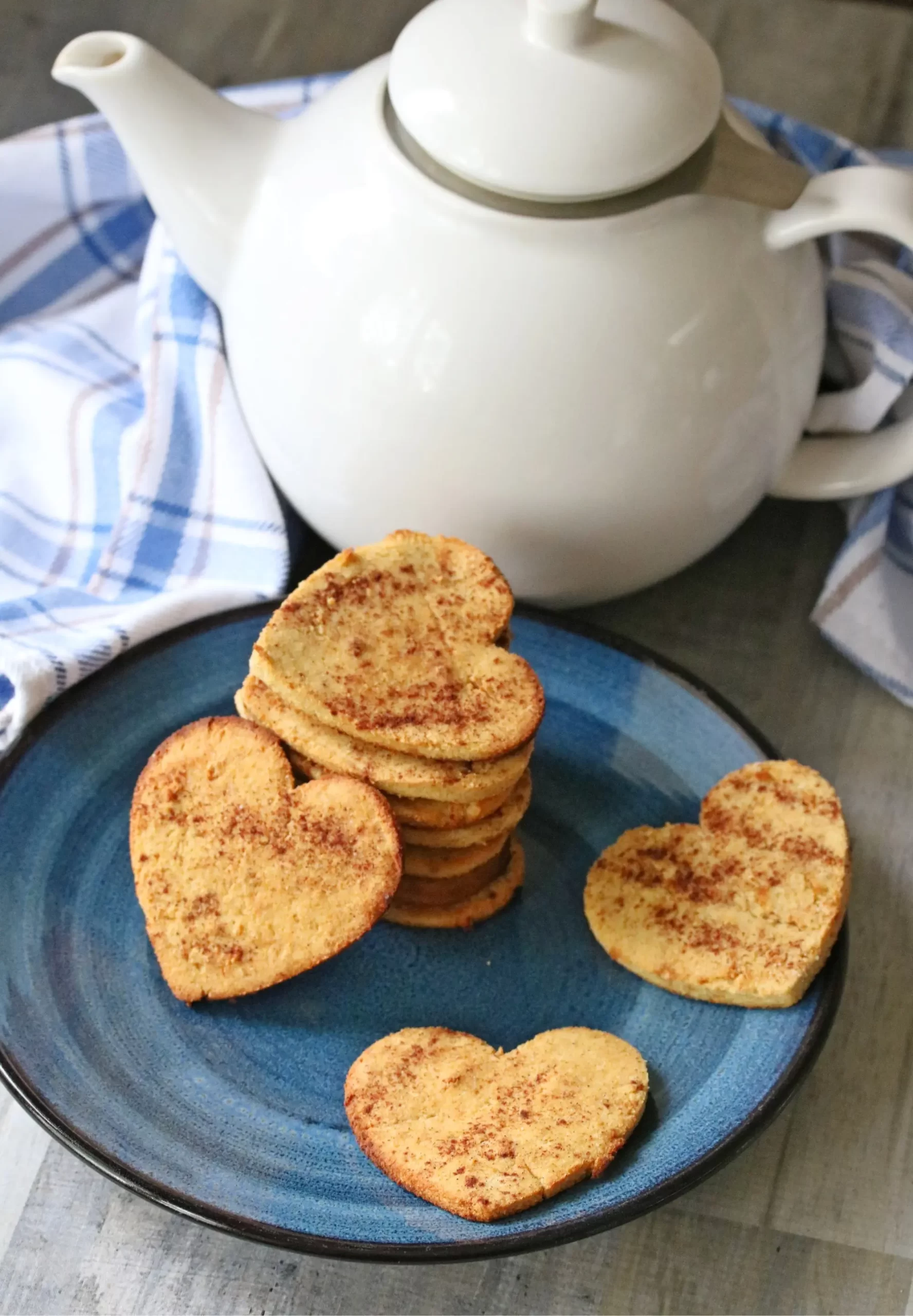 Heart cookies in a blue plate with a white teapot in the background.