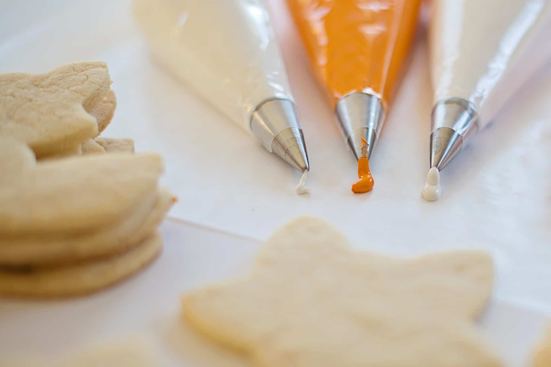 Three piping bags filled with icing and star shaped cookies.