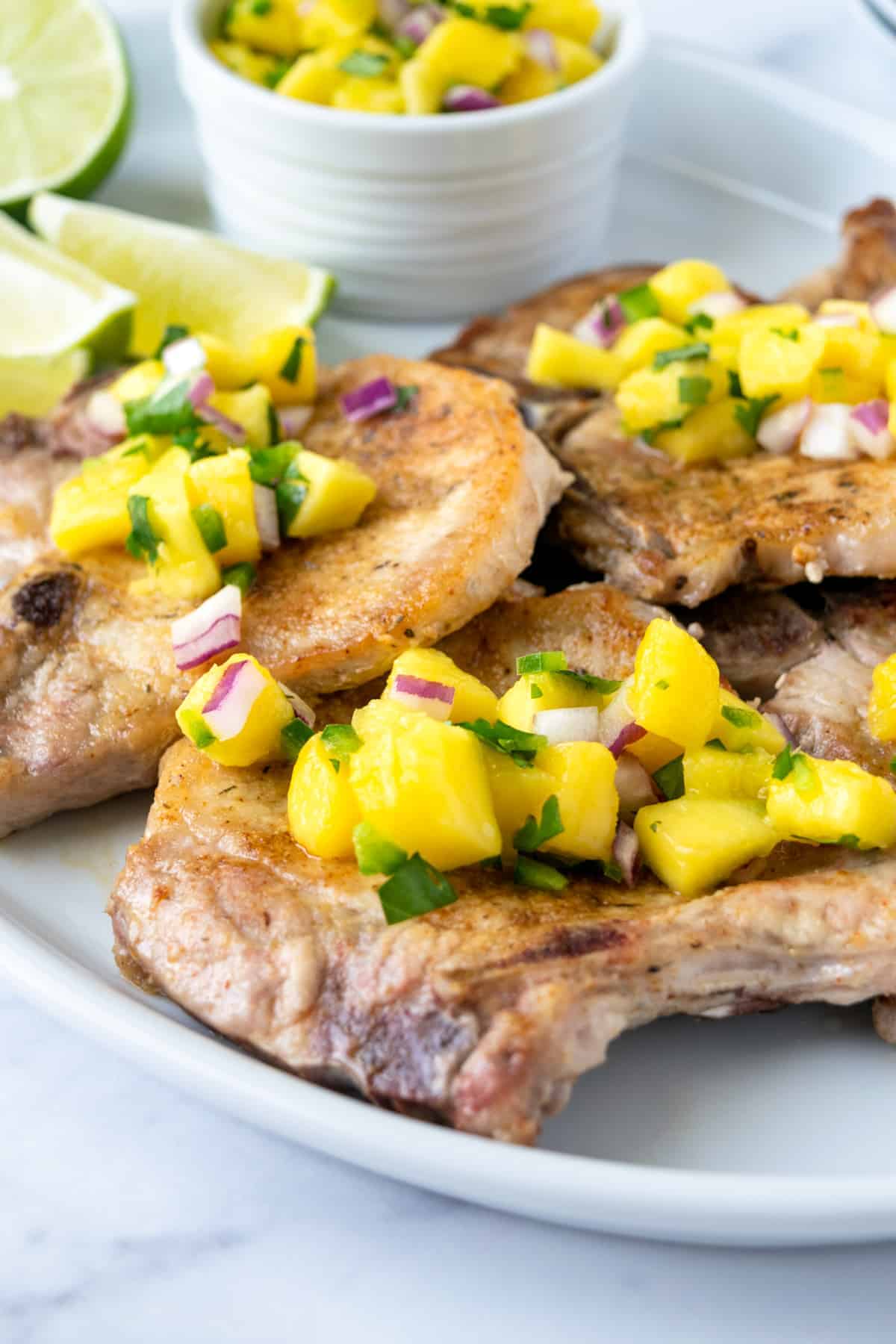 Pork chops garnished with mango salsa on a white platter.
