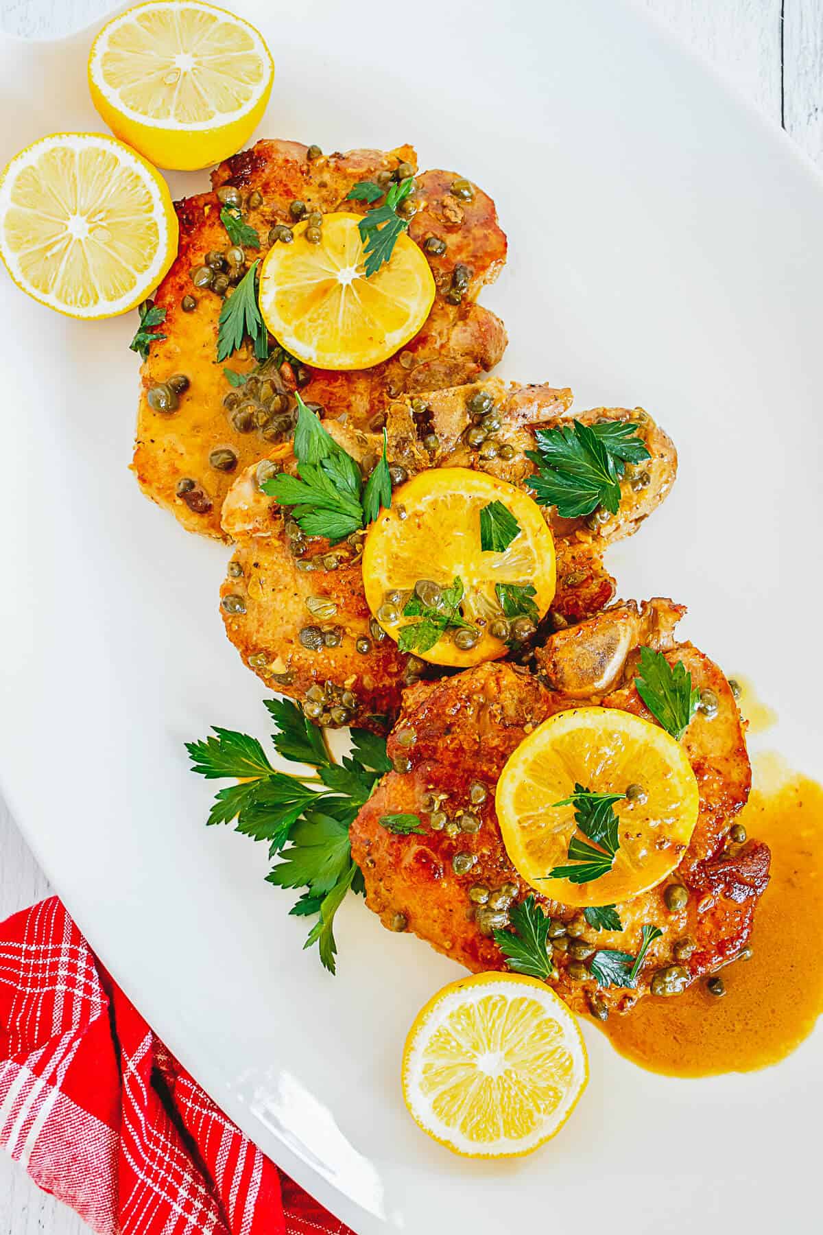 Pork piccata on a white platter served with slices of lemon.